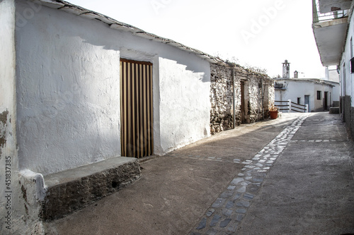 Laroles street with whitewashed walls with a door and bench attached to the facade and a typical Alpujarra fireplace in the background