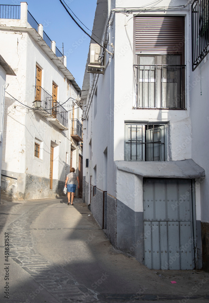 Laroles of the Alpujarras street with a small blue door in front and in the background a woman walking