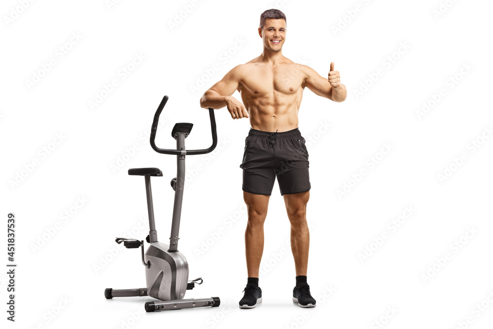 Shitless fit man leaning on an exercise bike and gesturing a thumb up sign Shitless fit man leaning on an exercise bike and gesturing a thumb up sign