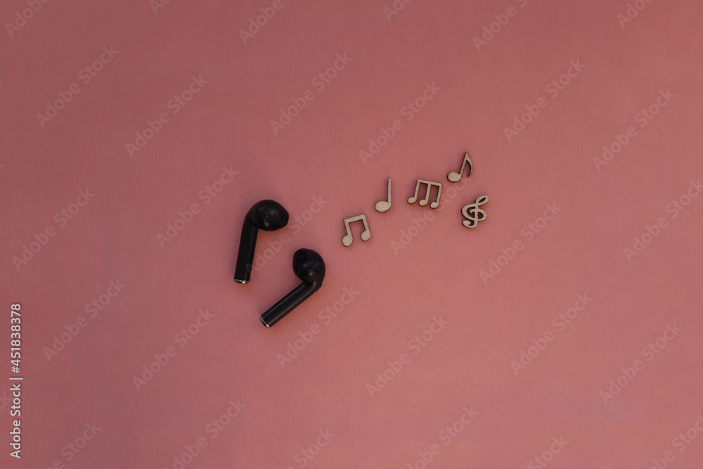 Wireless headphones are black, wooden notes on a pink background. Listening to songs, melodies, music.