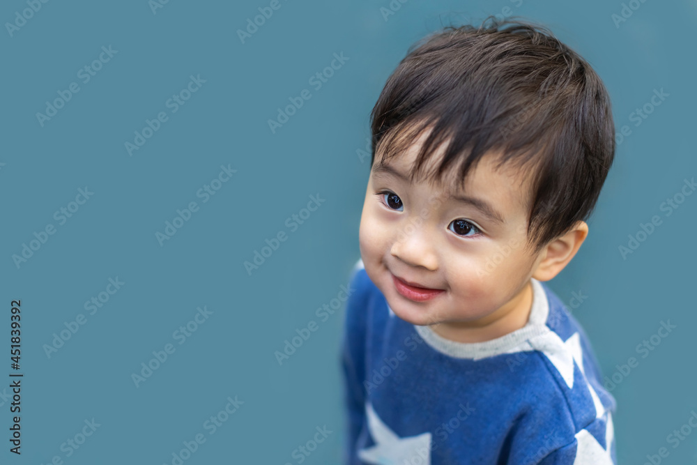 Happy little Asian boy looks away with a smile on blue background. Copy space for text