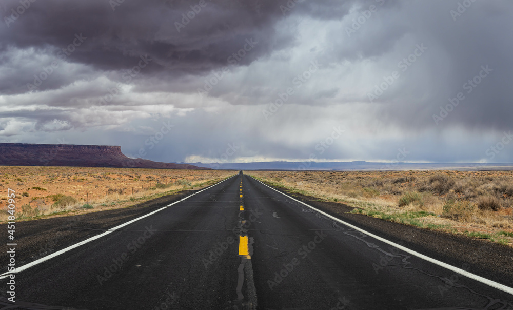 A straight road to the distant horizon across the desert of northern Arizona with the Vermillion Cliffs National Monument in the distance