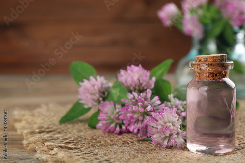 Beautiful clover flowers and bottle of essential oil on wooden table  closeup. Space for text