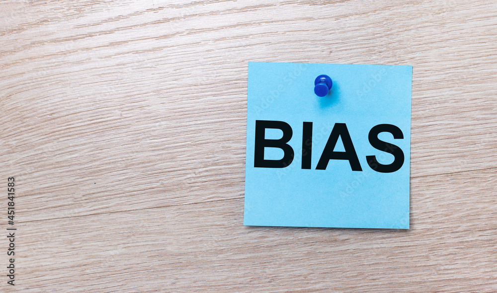 On a light wooden background - a light blue square sticker with the text BIAS On a light wooden background - a light blue square sticker with the text BIAS