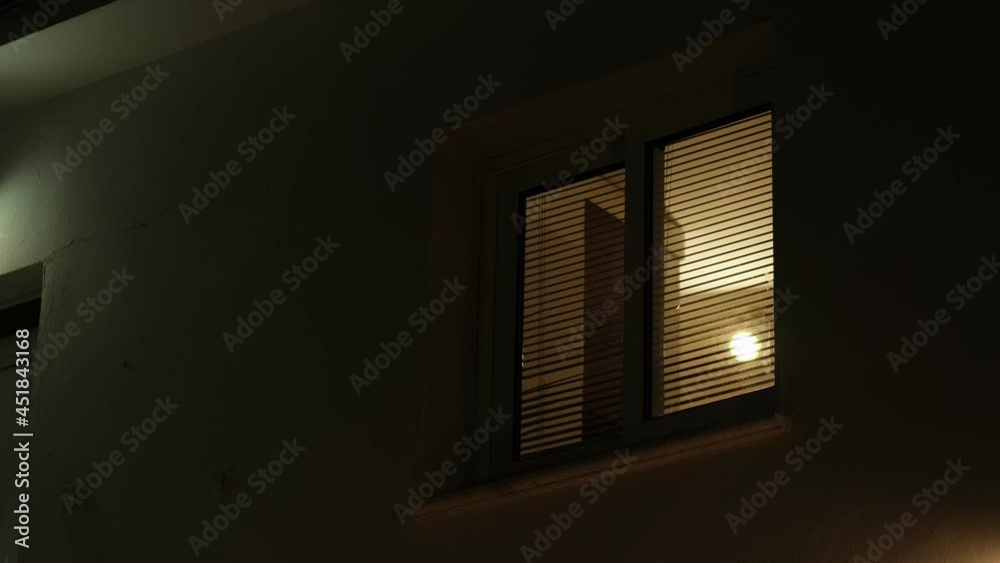 Light from the window of the house in the dark evening time. room lights up then turns off.