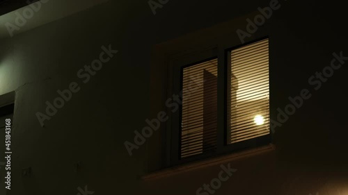 Light from the window of the house in the dark evening time. room lights up then turns off.