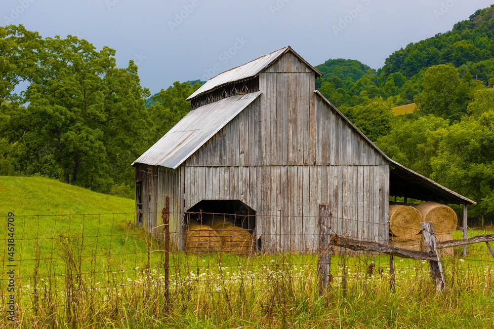 Fototapeta premium Barn full of rolled gray hay sits on hillside pasture in rural Virginia