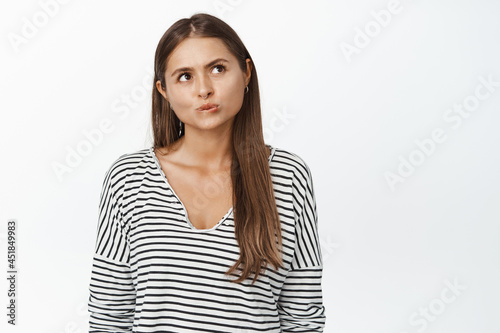 Young thoughtful female model looking aside with serious thinking face, white background © Cookie Studio