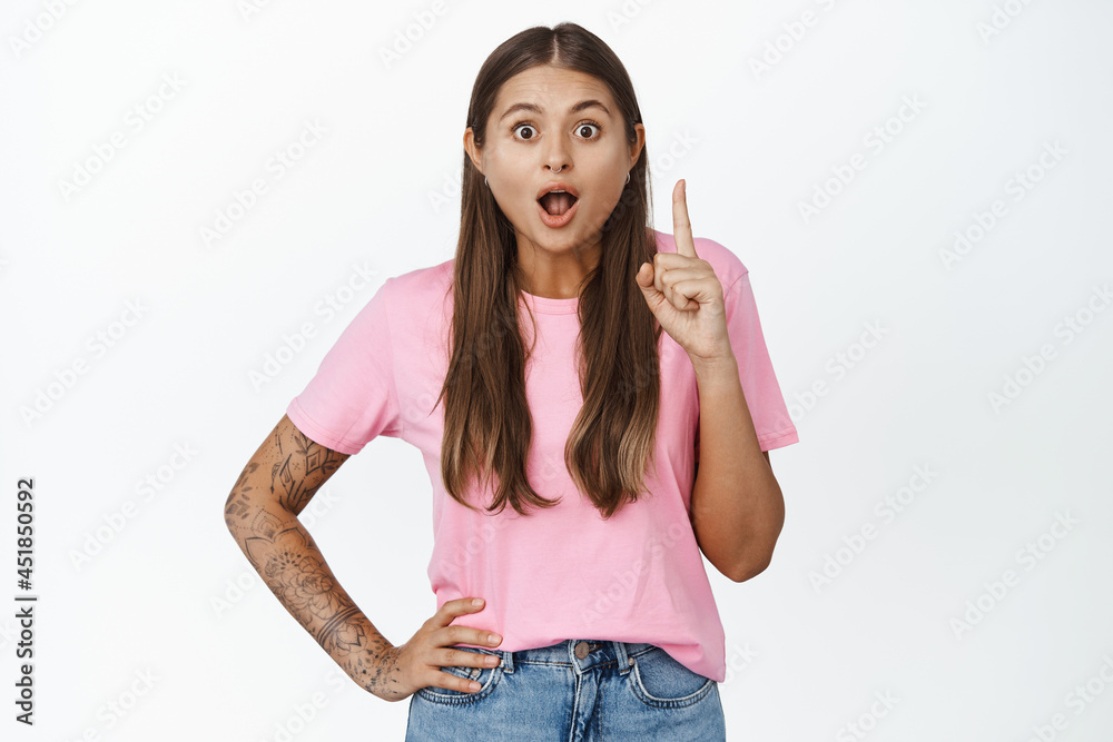Excited girl saying something with raised finger, pitching an idea, eureka gesture, standing amazed against white background Excited girl saying something with raised finger, pitching an idea, eureka gesture, standing amazed against white background