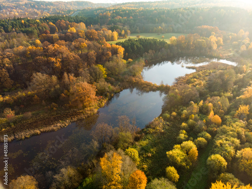 Birds eye view of autumn forest and a small lake. Aerial colorful forest scene in autumn with orange and yellow foliage.