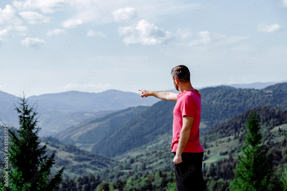 Man points his hand towards mountains. unrecognizable man from the back stands in front of mountain landscape and blue sky
