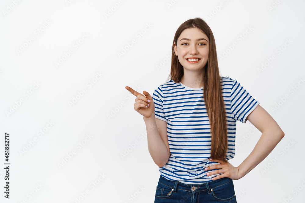 Young smiling girl pointing finger left, looking happy and satisfied, showing sale banner on copy space, standing against white background Young smiling girl pointing finger left, looking happy and satisfied, showing sale banner on copy space, standing against white background