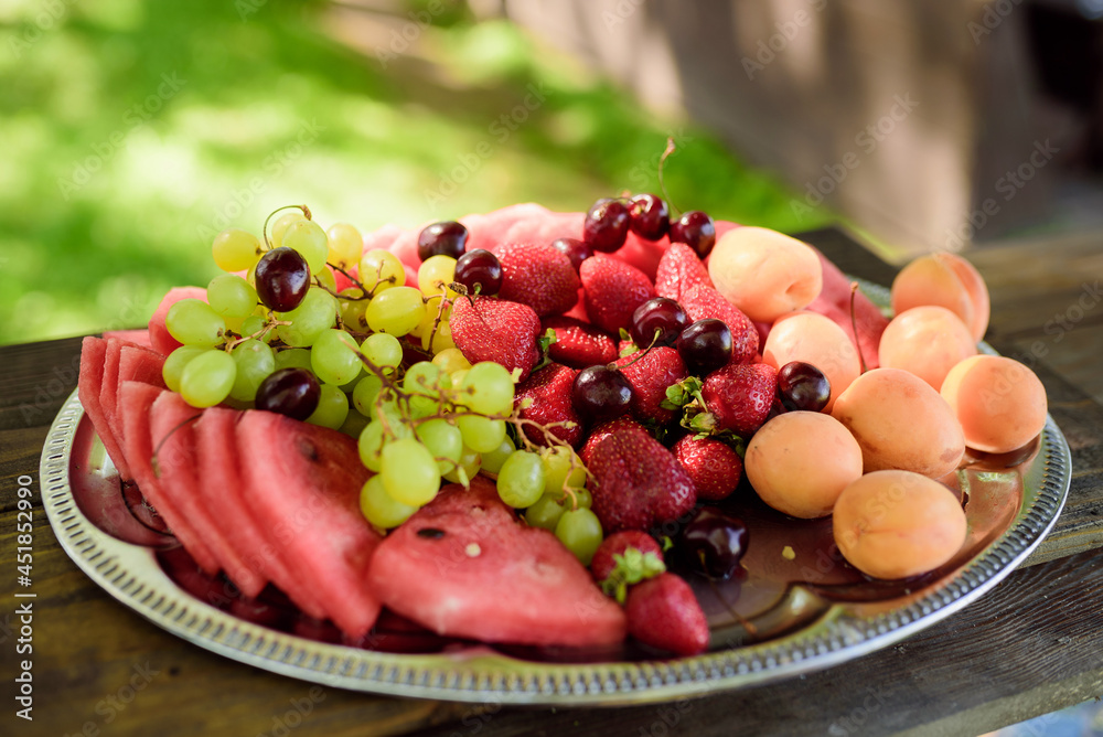 There is a plate of fruit on a wooden table outside There is a plate of fruit on a wooden table outside