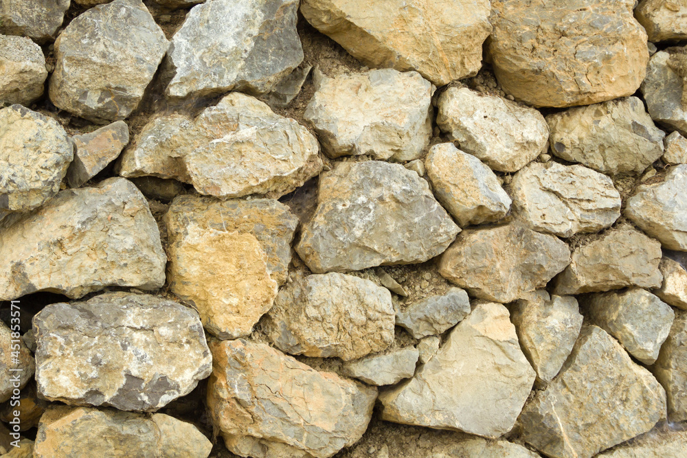 Frontal view of a wall made of brown, untreated stones, fastened with soil. .Texture, background.