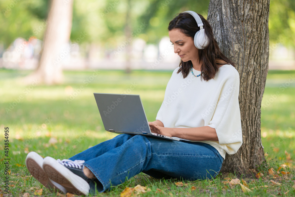 Portrait of a 40-years-old woman with laptop in city park during online vido call. Online working concept or concept of a distant online education. Portrait of a 40-years-old woman with laptop in city park during online vido call. Online working concept or concept of a distant online education.