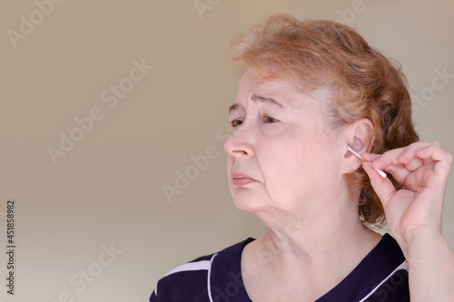 an elderly Caucasian woman cleans her ear with a cotton swab