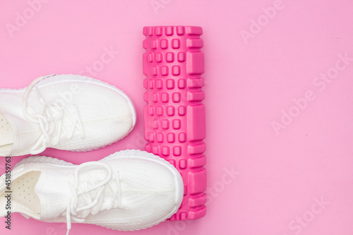 The concept of fitness. Pink fitness roller for training. Sneakers. Women's fitness at home.