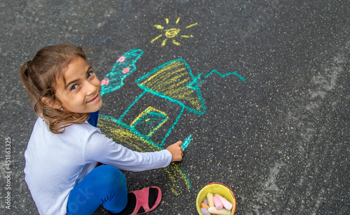 The child draws with chalk on the asphalt. Selective focus.