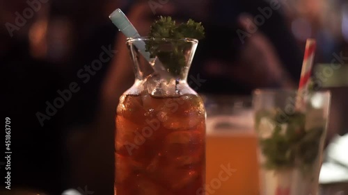 panning shot of a glass flask with a straw filled with ice and with droplets of condensation filled with alcoholic beverage long island iced tea LIIT showing the opening up social hotspots like photo