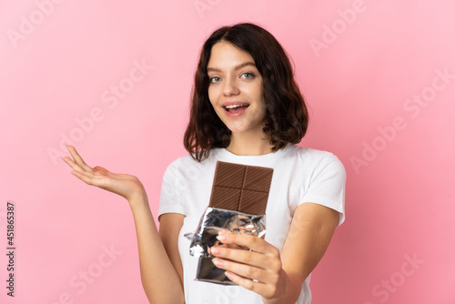 Teenager Ukrainian girl isolated on pink background taking a chocolate tablet and surprised