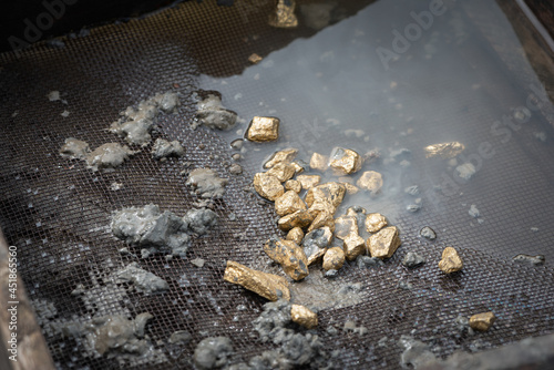 Golden ore in the dirty metal grid in the river water. Sifting gold concept.