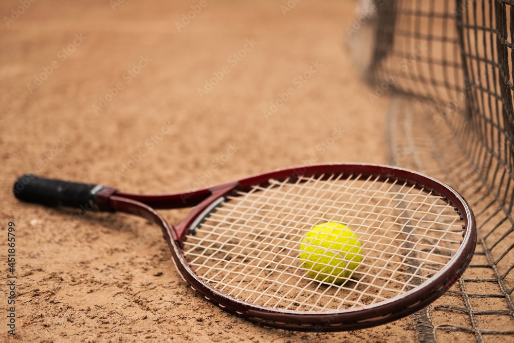 A bright yellow tennis ball and a tennis racket lie near the court net.