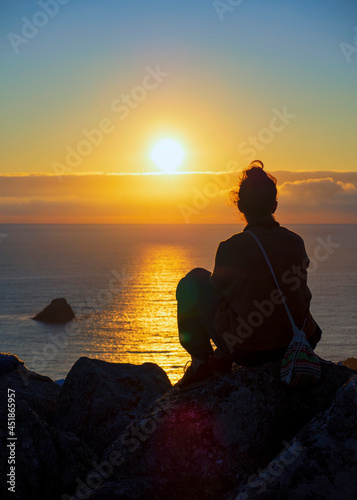 Chica joven disfrutando de la puesta de sol en el cabo de Finisterre photo