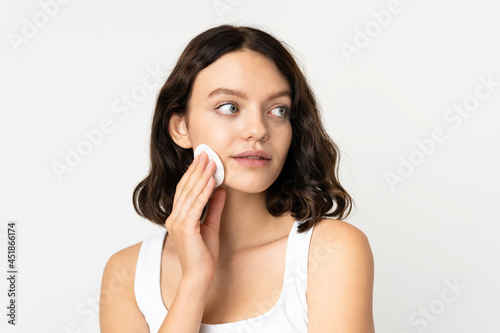 Teenager Ukrainian girl isolated on white background with cotton pad for removing makeup from her face
