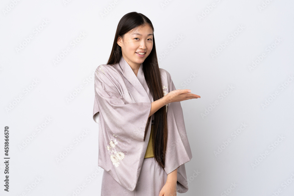 Young Chinese girl wearing kimono over isolated background presenting an idea while looking smiling towards Young Chinese girl wearing kimono over isolated background presenting an idea while looking smiling towards