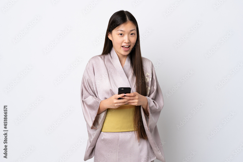 Young Chinese girl wearing kimono over isolated background surprised and sending a message Young Chinese girl wearing kimono over isolated background surprised and sending a message