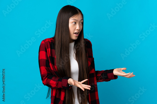 Young Chinese girl over isolated blue background with surprise expression while looking side