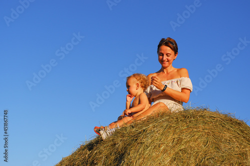 Little boy with mom on a haystack. Mom with baby on a background of blue sky. Mom with a small child on a pile of hay