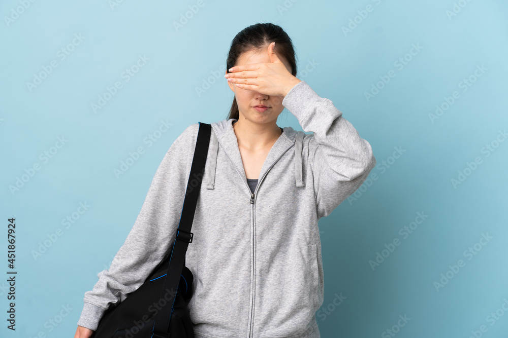 Young sport Chinese woman with sport bag over isolated blue background covering eyes by hands. Do not want to see something Young sport Chinese woman with sport bag over isolated blue background covering eyes by hands. Do not want to see something