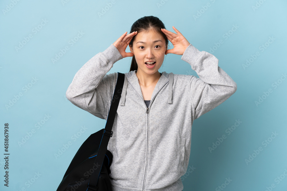 Young sport Chinese woman with sport bag over isolated blue background with surprise expression Young sport Chinese woman with sport bag over isolated blue background with surprise expression