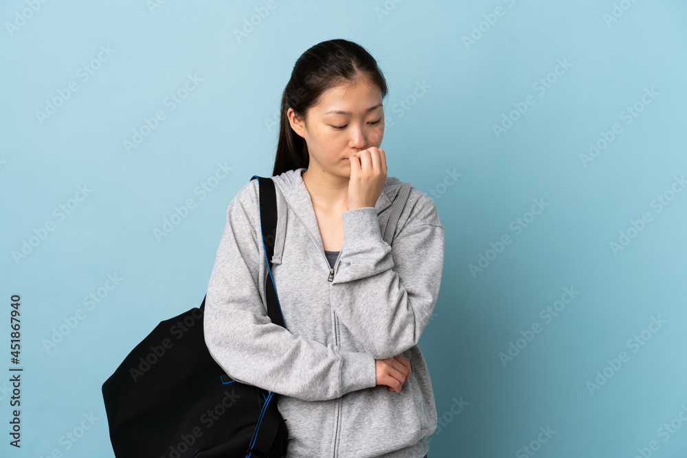 Young sport Chinese woman with sport bag over isolated blue background having doubts Young sport Chinese woman with sport bag over isolated blue background having doubts
