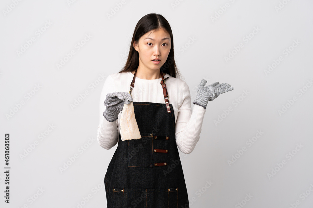 Chinese fishmonger wearing an apron and holding a raw fish over isolated white background making doubts gesture Chinese fishmonger wearing an apron and holding a raw fish over isolated white background making doubts gesture