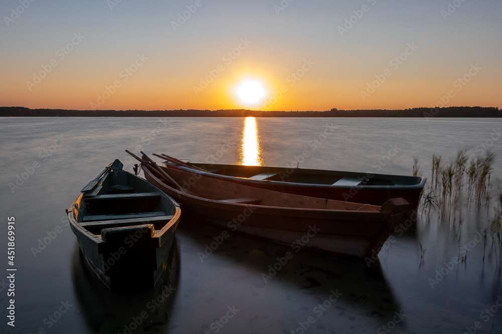 Three wooden fishing boats near the shore, in the background sunset.