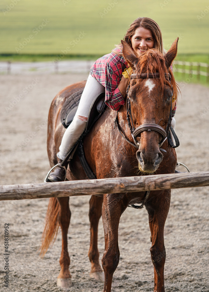 Obraz premium Young woman in shirt resting on brown horse after ride leaning forward, smiling - his coat wet from sweat