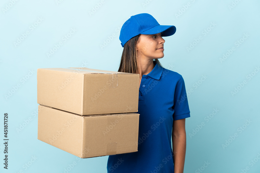 Young delivery woman isolated on blue background looking to the side Young delivery woman isolated on blue background looking to the side