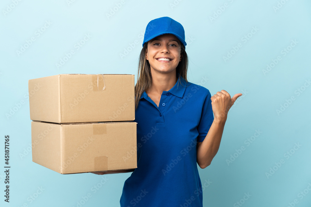 Young delivery woman isolated on blue background pointing to the side to present a product