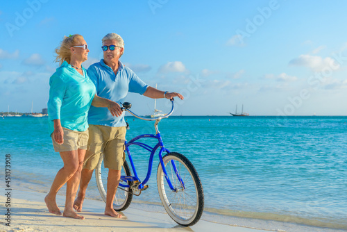 Happy senior couple exercising with bicycles on the beach on a sunny day