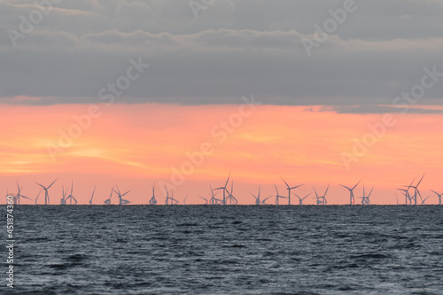 Wind farm in the Irish Sea at dusk. A mirage effect causes the turbines on the horizon to appear to bend as they rotate