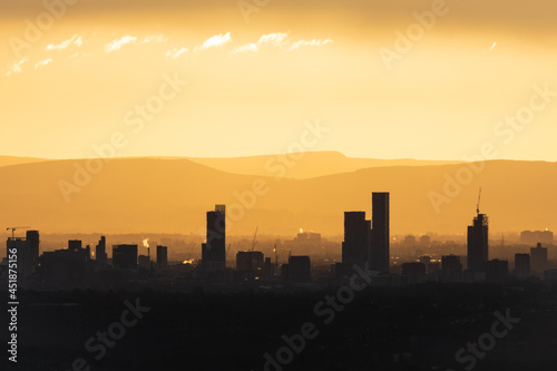 Manchester city skyline silhouetted against the sunrise, the tower blocks and buildings are visible against the yellow morning glow