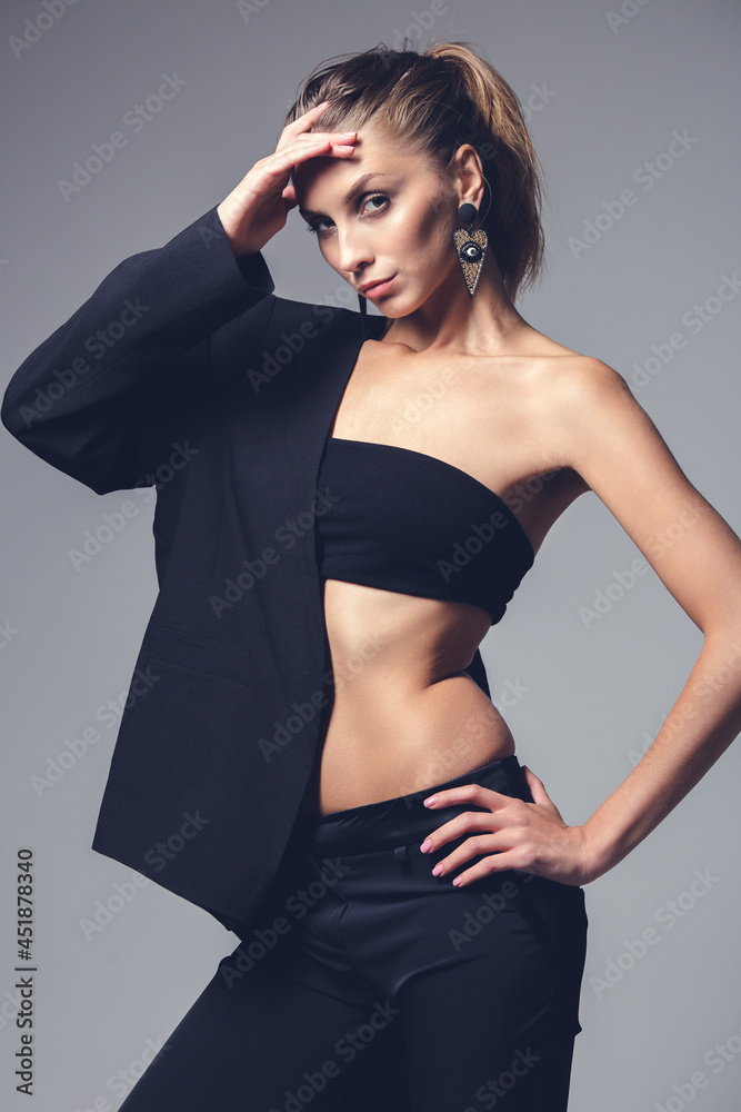 Fototapeta premium Slim girl on in a black top on a gray studio background. Slim model posing in the studio. Contrasting light