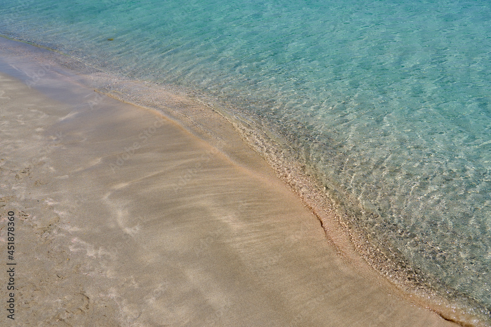 Clear waves and colorful sand on tropical sandy beach in Crete Greece.