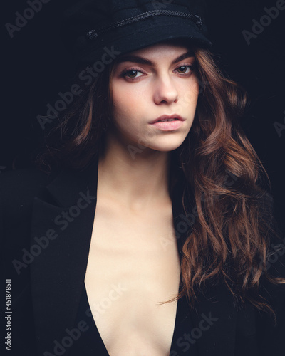 Fashionable studio portrait of a beautiful young model in black hat and sexy top on a black background. Low key.