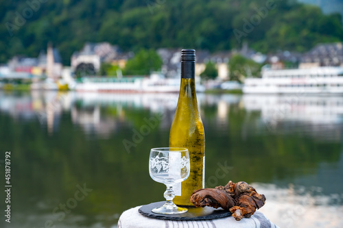 Tasting of white quality riesling wine served on outdoor terrace in Mosel wine region with Mosel river and old German town on background, Germany