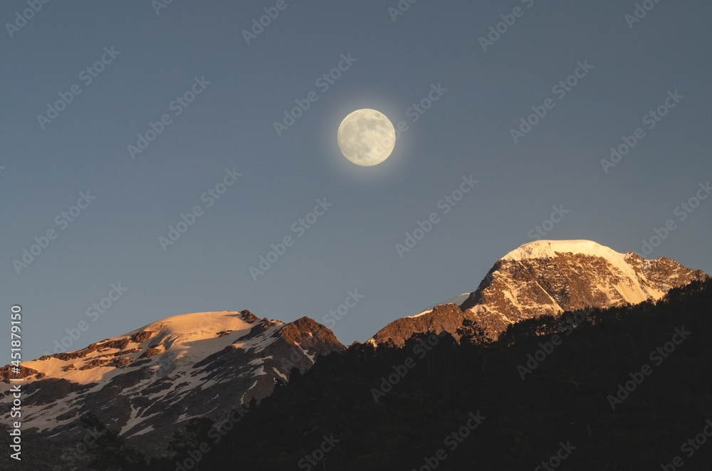 Full moon in the mountains. The moon illuminates the snowy peaks of the mountains. Full moon in the mountains. The moon illuminates the snowy peaks of the mountains.