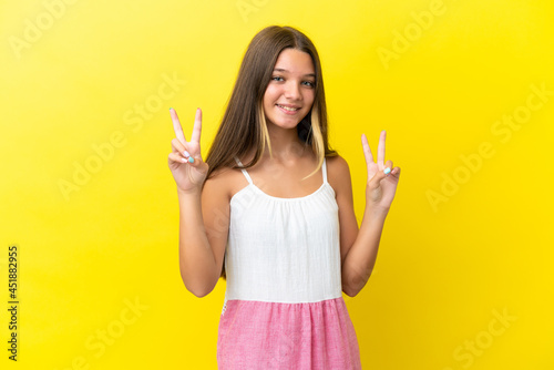 Little caucasian girl isolated on yellow background showing victory sign with both hands