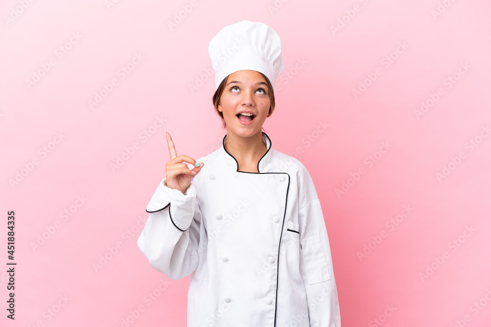 Little caucasian chef girl isolated on pink background pointing up and surprised Little caucasian chef girl isolated on pink background pointing up and surprised